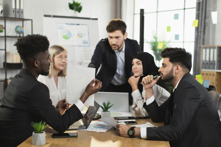 Kommunikation im Team Fünf Personen in geschäftlicher Kleidung bei einer Teamdiskussion am Tisch.