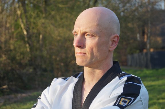 Kampfkunst: Ruhe Markus Koschorreck im Taekwondo-Anzug mit schwarzem Kragen blickt ruhig und fokussiert schräg zur Seite.