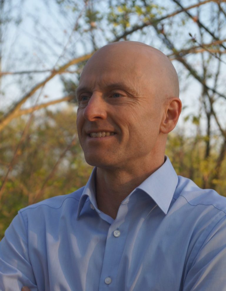 Dr. Markus Koschorreck lächelnd von schräg vorne vor Bäumen in der Abendsonne.