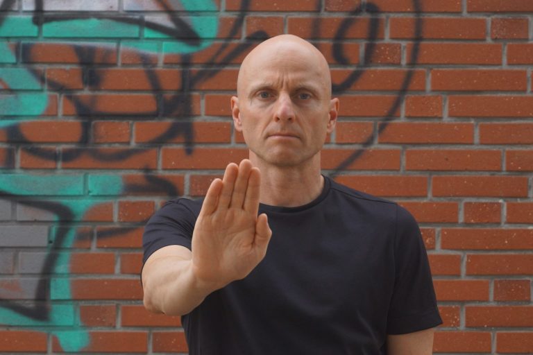 Selbstbehauptung Dr. Markus Koschorreck zeigt mit erhobener Hand und entschlossenem Blick ein klares Stoppzeichen. Im Hintergrund eine Wand mit Graffiti.