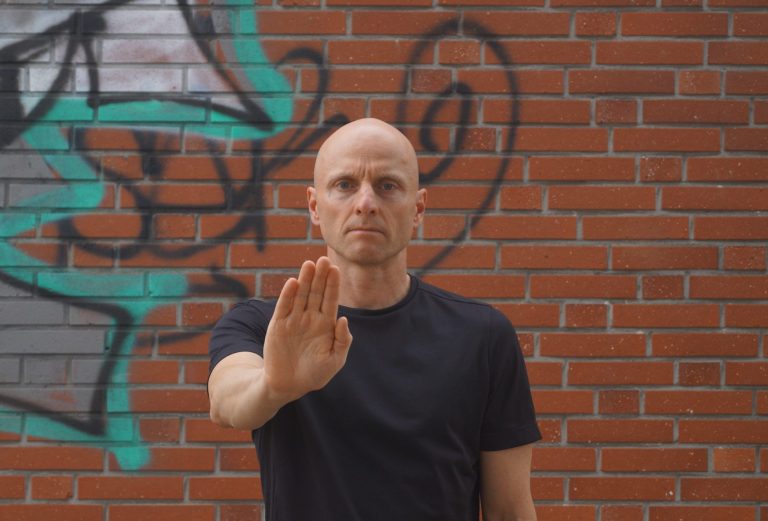 Markus Koschorreck mit nach vorne ausgestreckter Hand vor Wand mit Graffiti.