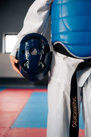 Schutzausrüstung Ein Taekwondo-Kämpfer mit Schutzausrüstung im Trainingsraum. Seitlicher Ausschnitt Rumpf mit Beine.